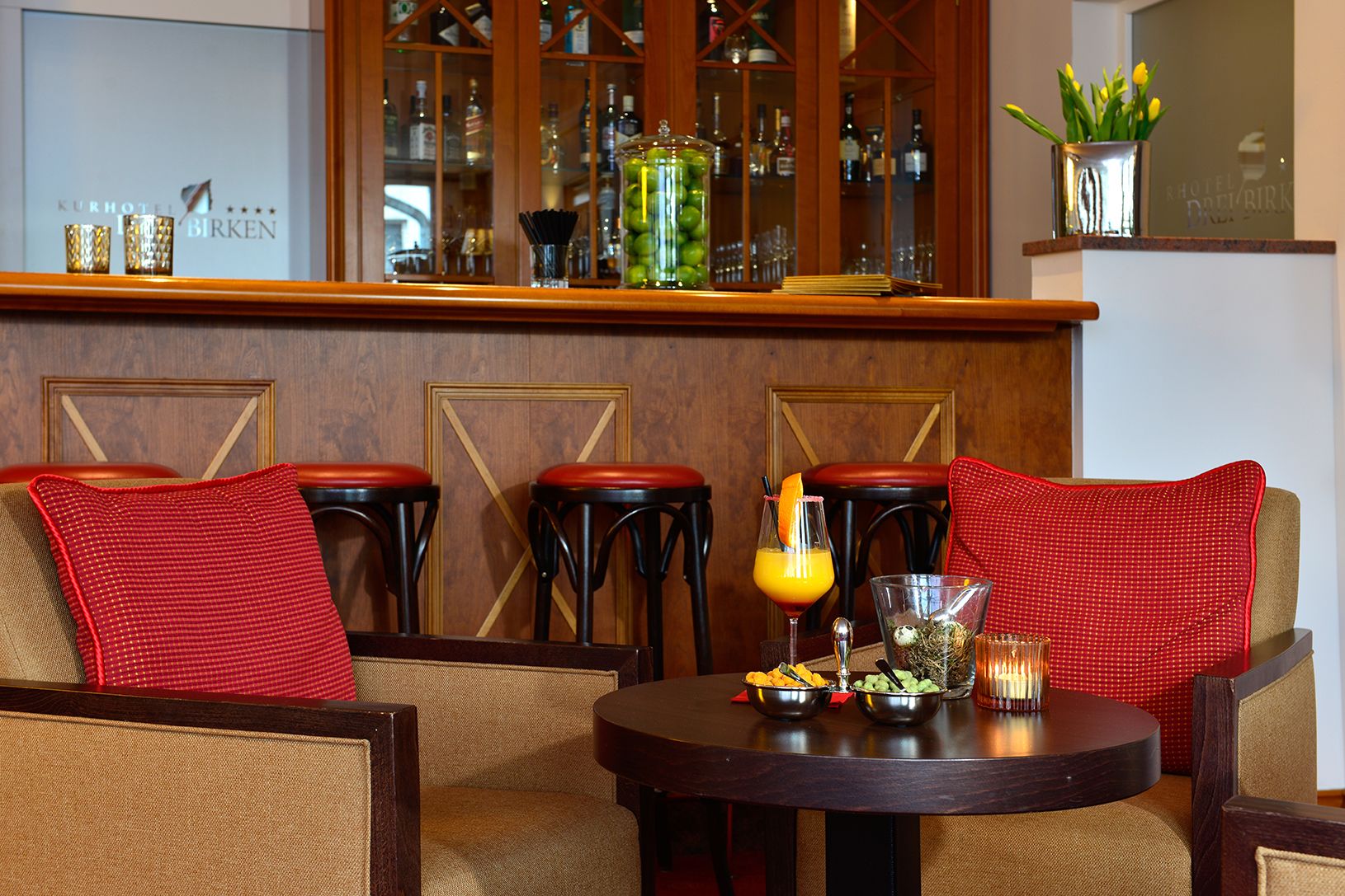 Eine Bar mit Holzwandverkleidung, einer Minibar und einer Sitzecke mit roten Kissen.