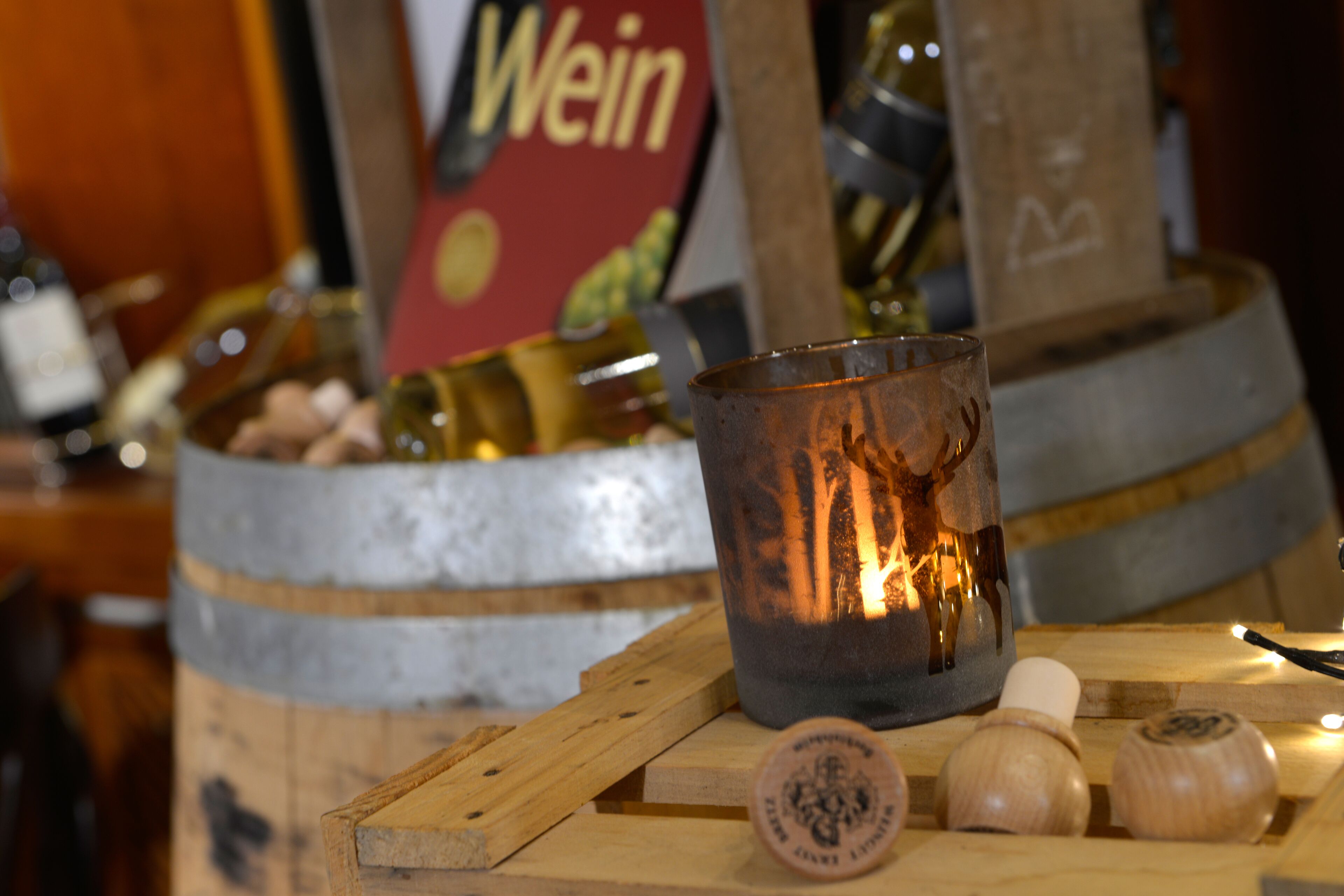 Una candela in un portacandela su una superficie di legno, con botti e un cartello sullo sfondo.