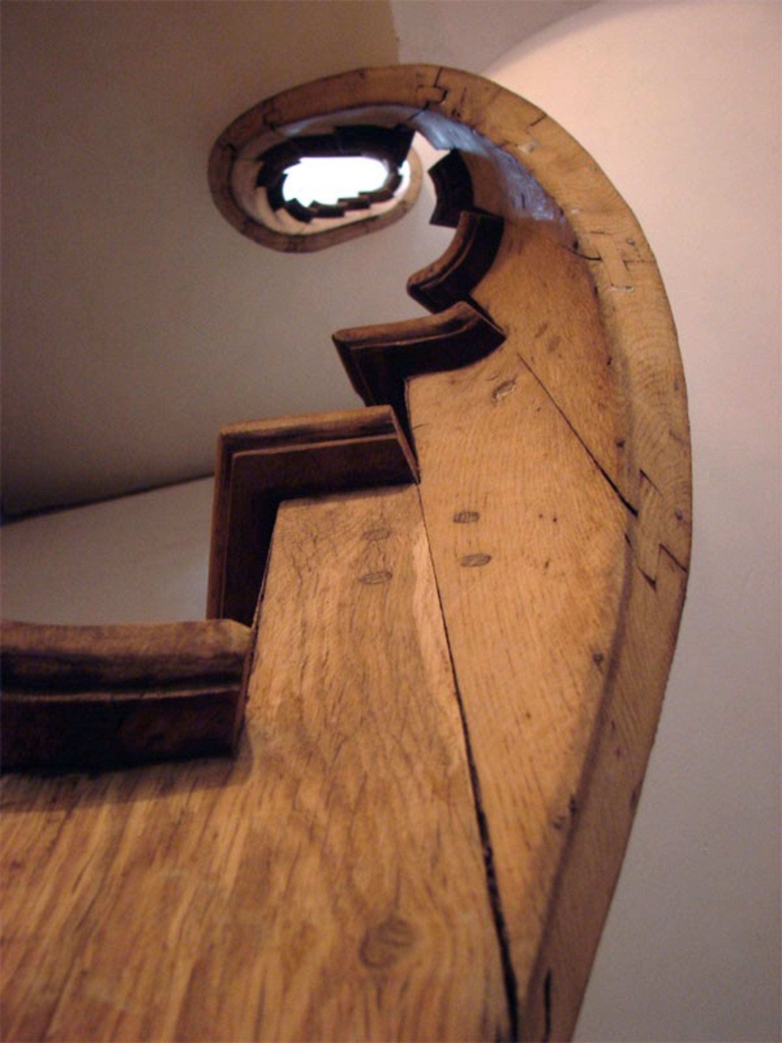A wooden staircase with a circular cutout at the top, leading to a higher floor.
