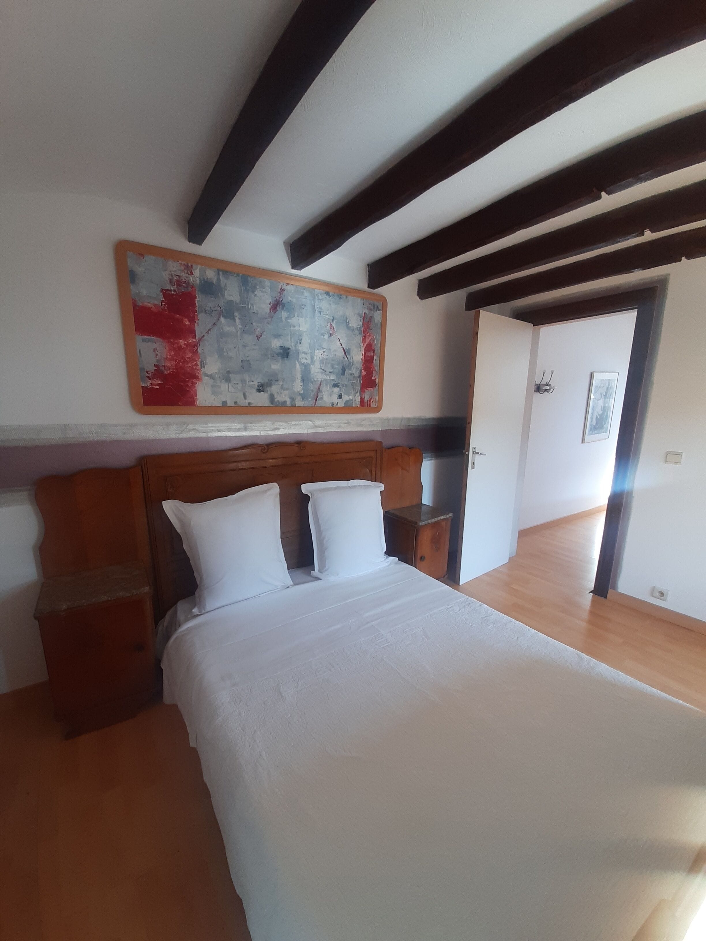 Un dormitorio con cabecera de madera, una cama grande con ropa de cama blanca, una mesita de noche y un cuadro sobre la cama.