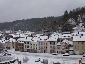 A snow-covered town with multi-story buildings, a main road, and a hilly backdrop.