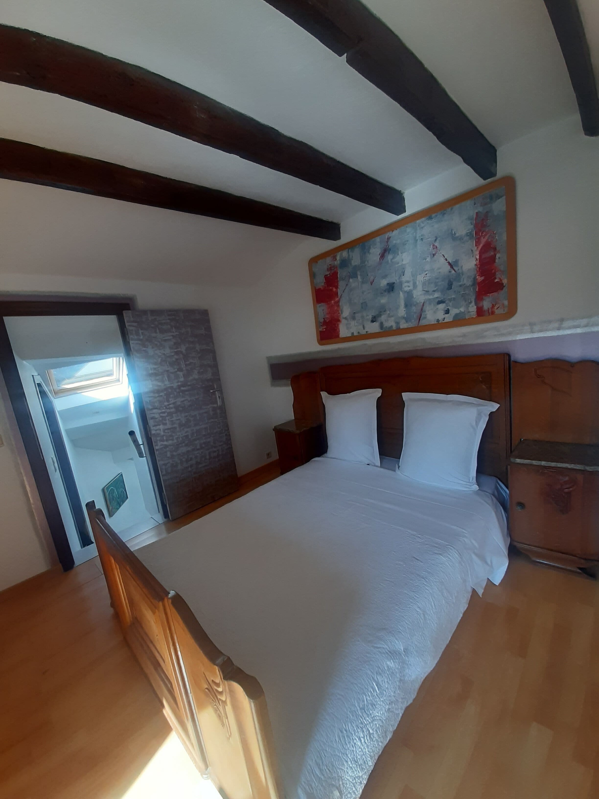 Un dormitorio con una cama grande, cabecera de madera, una mesita de noche, un aparador y un cuadro en la pared.