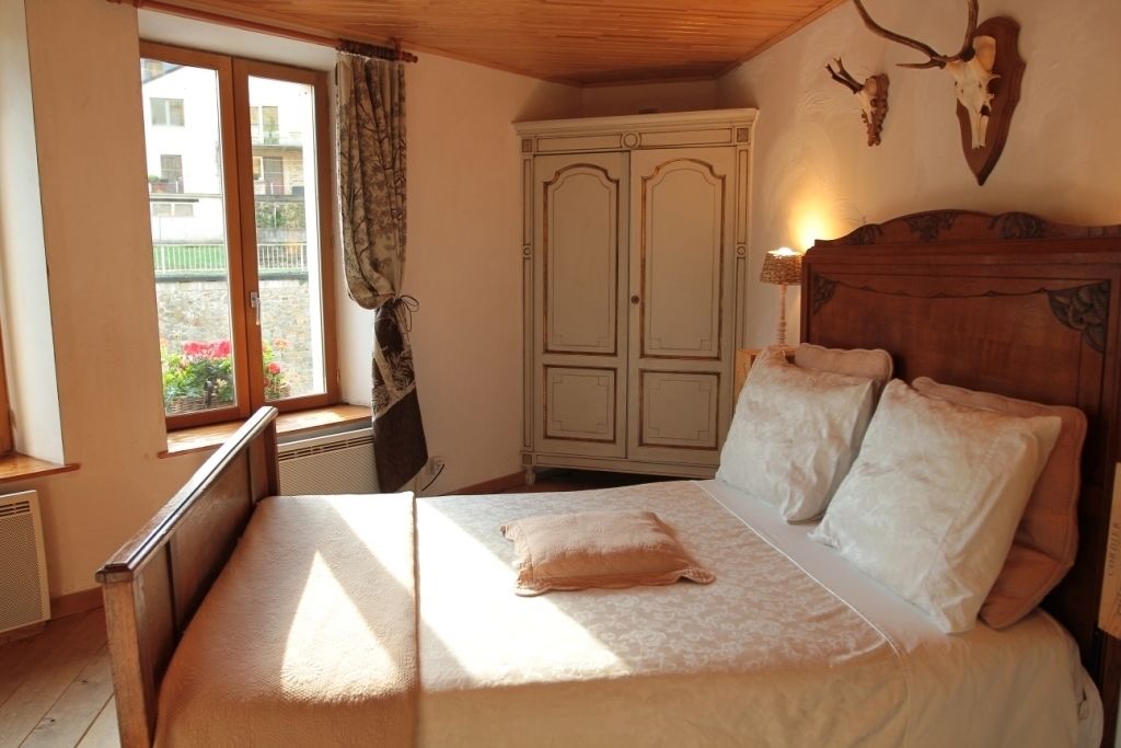 Une chambre avec un lit en bois, une fenêtre avec des rideaux, une armoire et une décoration murale représentant un crâne de cerf.