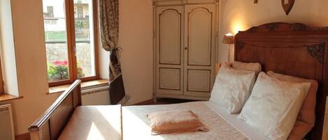 A bedroom with a wooden bed, a window with curtains, a wardrobe, and a wall-mounted deer skull decoration.