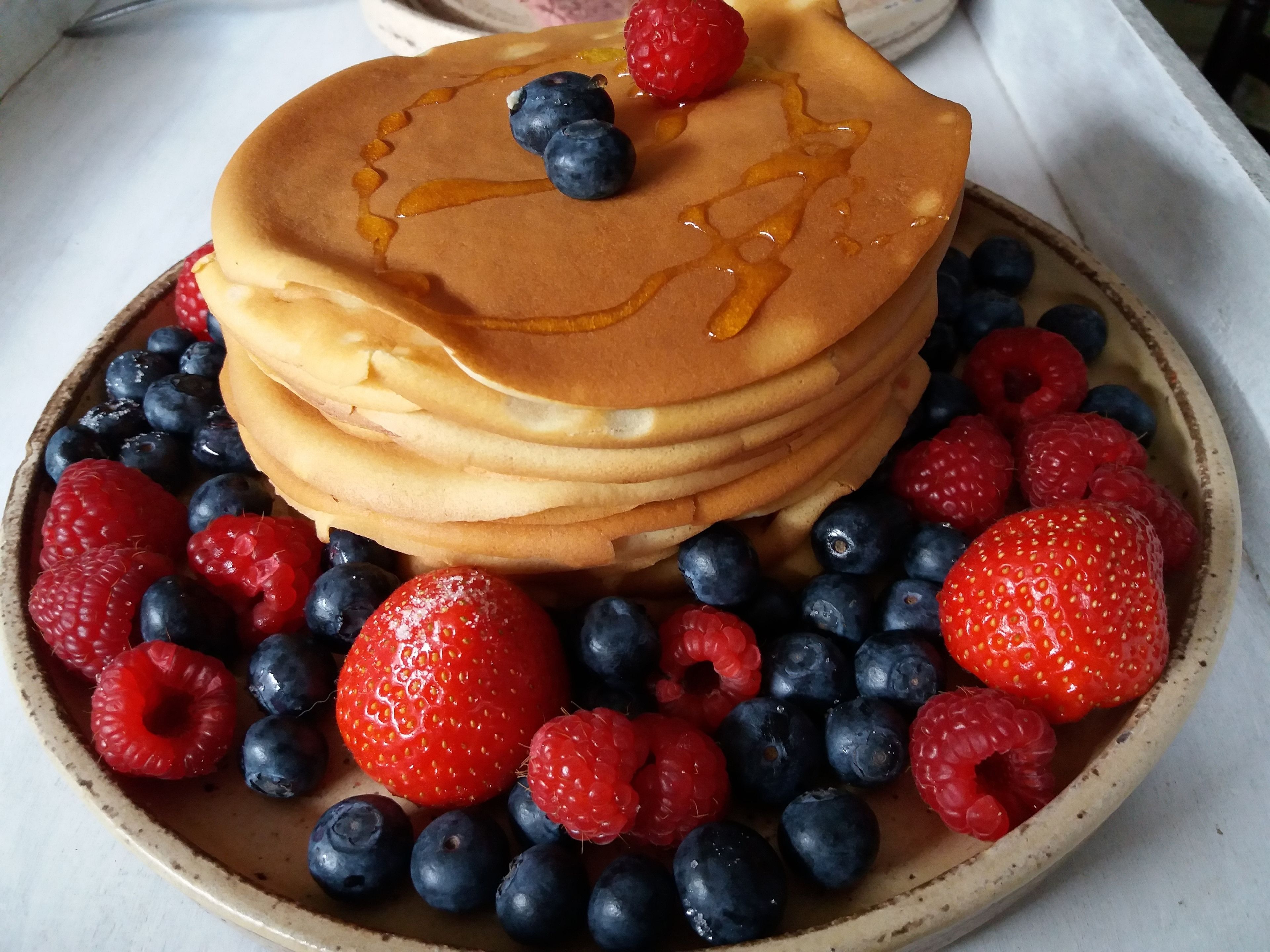 Una pila di pancake con sciroppo e frutti di bosco su un piatto.