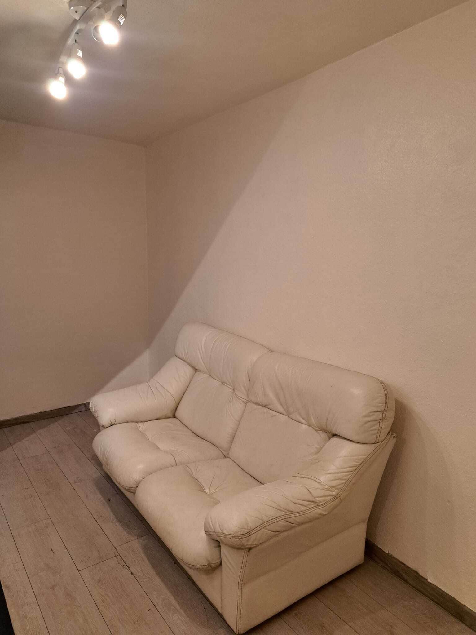 Un sofá de cuero color beige en un rincón de una habitación con suelo de madera y techo inclinado.
