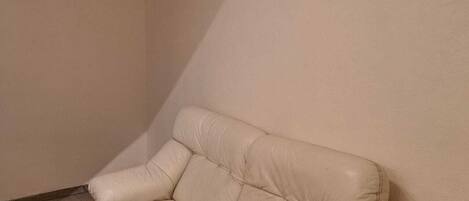 Un sofá de cuero color beige en un rincón de una habitación con suelo de madera y techo inclinado.