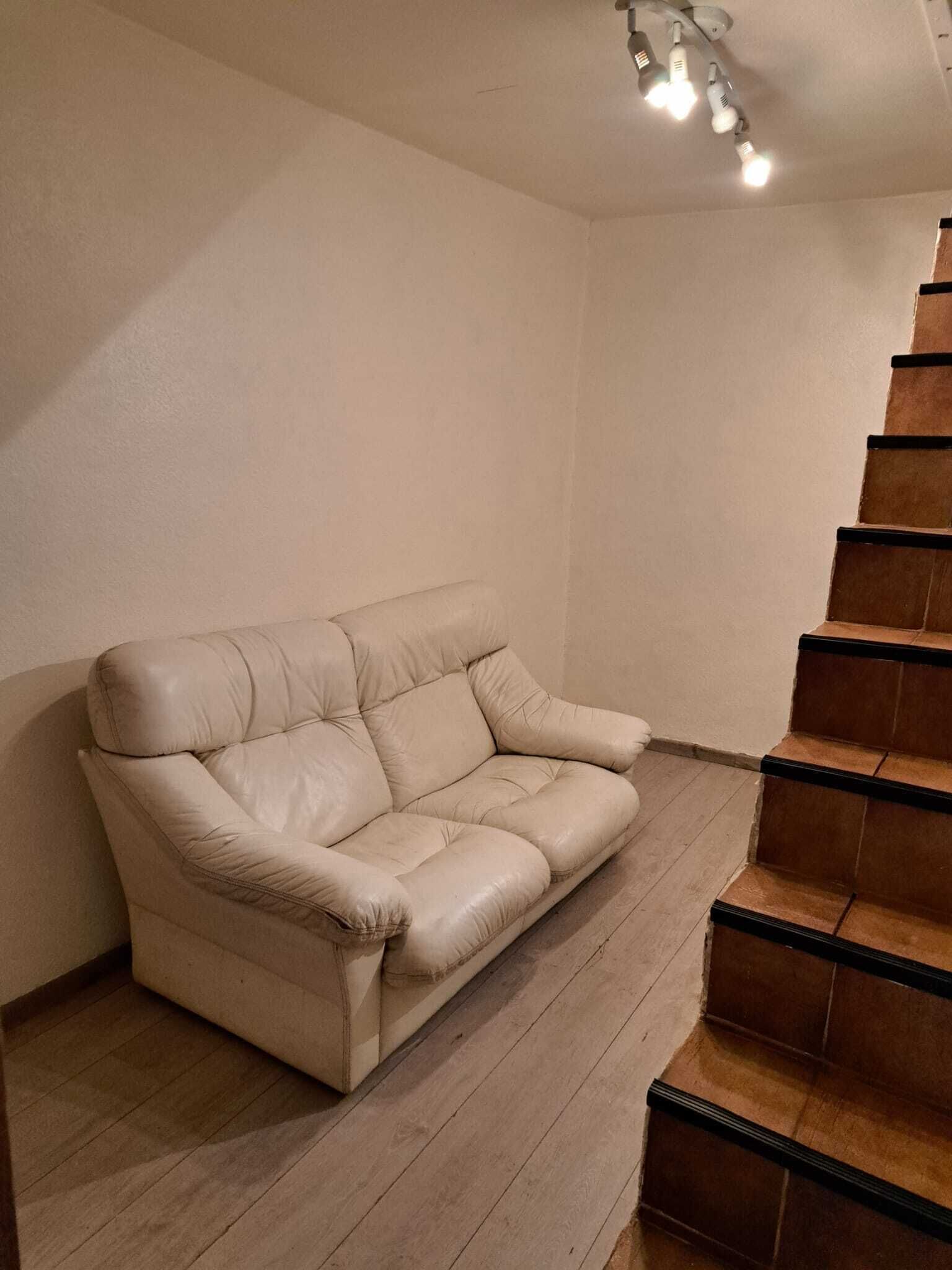 Um sofá de couro bege em frente a uma parede com uma escada de madeira.