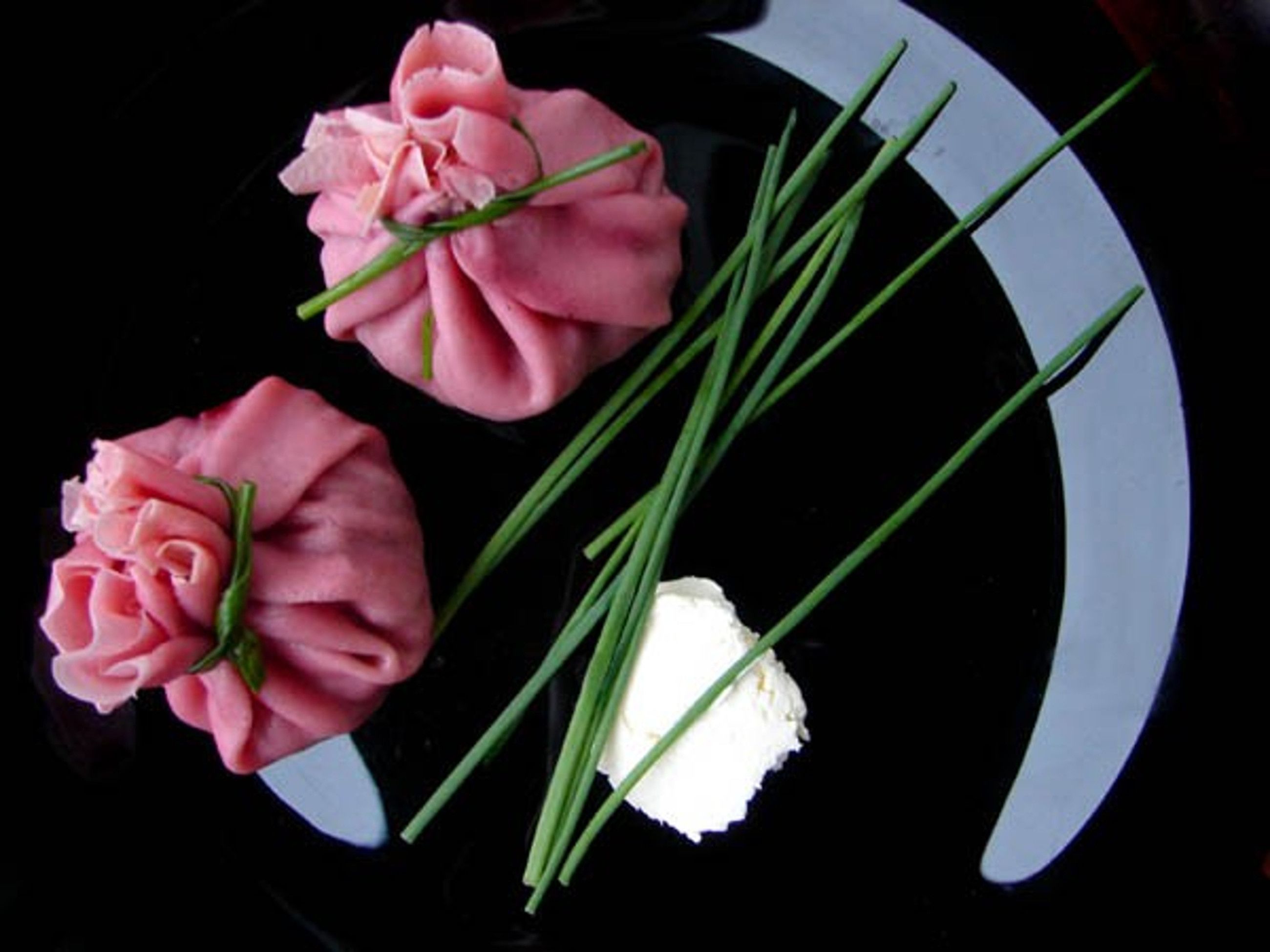 Un plato negro con tres rosas rosadas y varias cebollitas verdes.