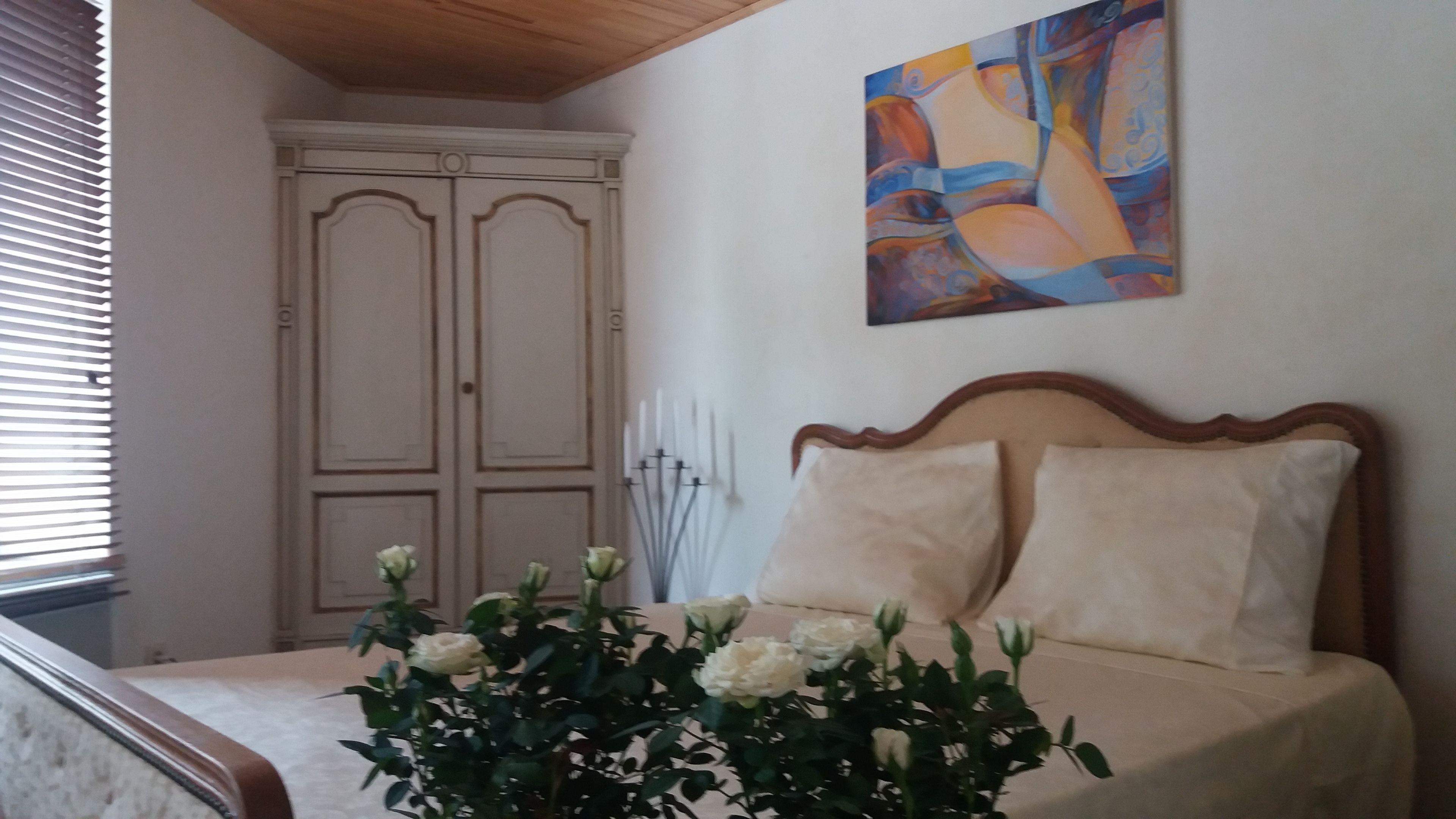 A bedroom with a bed, a painting, and a window with blinds.