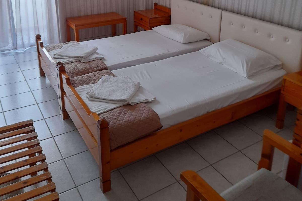 A hotel room with two single beds, a wooden nightstand, a small table, and a chair.