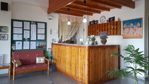 A reception area with a wooden counter, a sofa, a bulletin board, and a clock on the wall. - Phaethon Hotel (Kos)