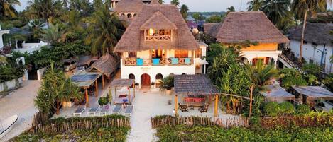 A hotel with a central building, multiple thatched-roof structures, and a beach area with sun loungers.
