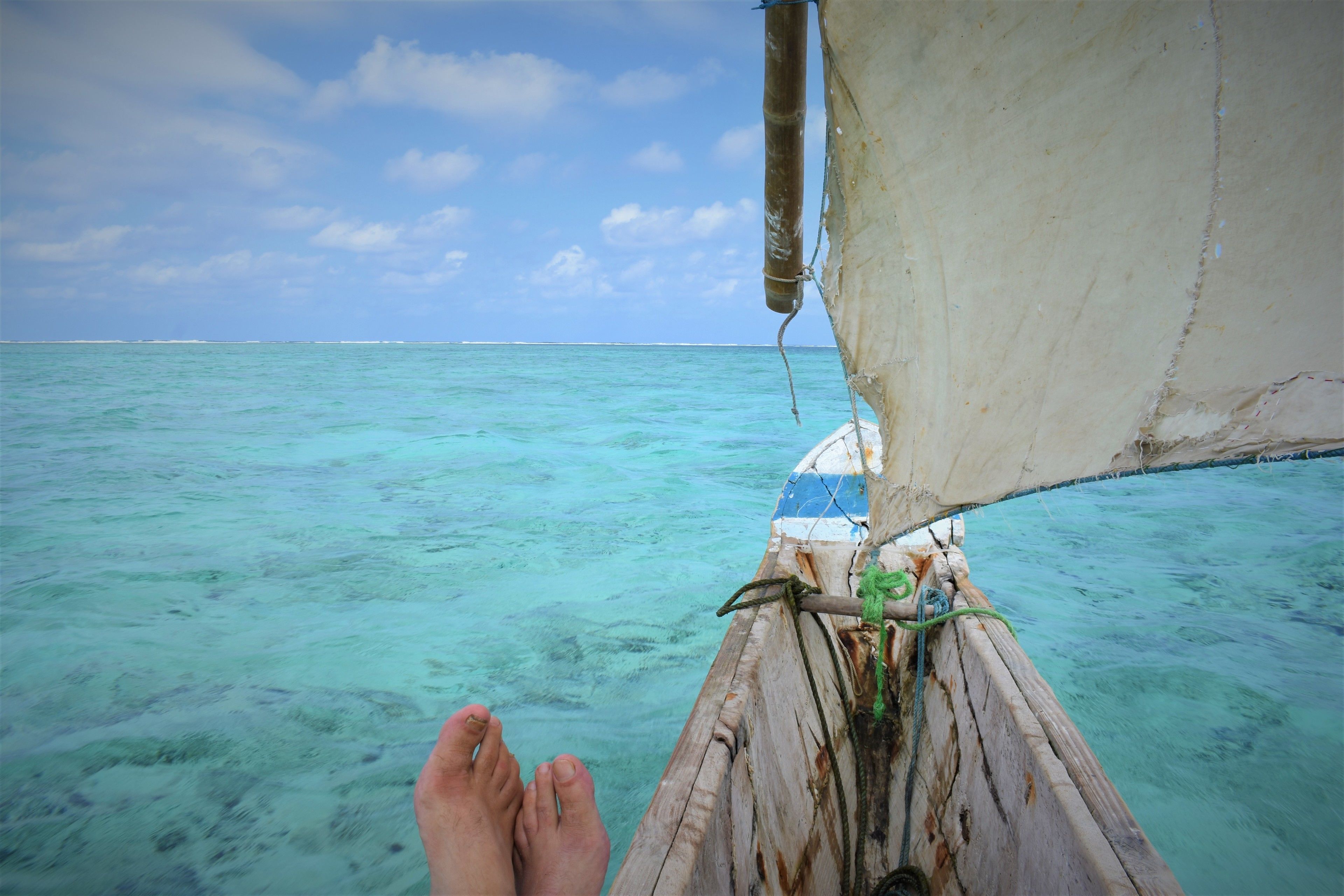 A boat's wooden bow with a person's feet resting on it, extending over turquoise water.