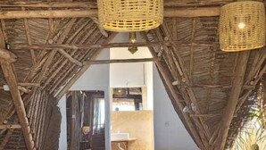 Une pièce rustique avec un banc en bois, des paniers tressés suspendus au plafond et un tapis en fibres naturelles sur le sol.