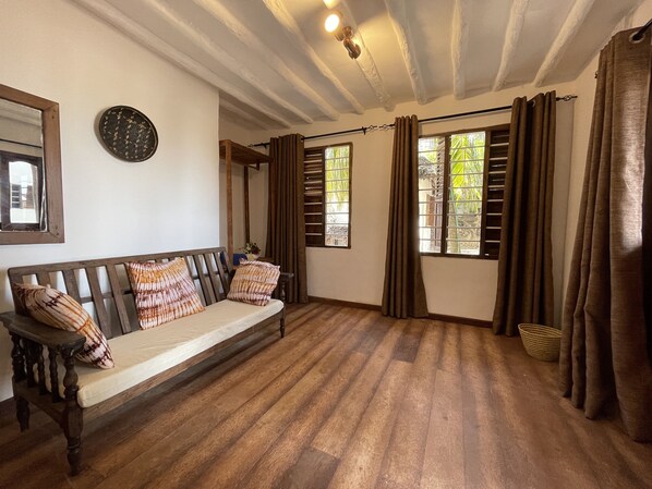Una habitación con un banco de madera, un reloj en la pared y un ventanal con cortinas.