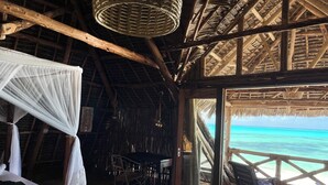 Une pièce avec un plafond en bois, un lit à baldaquin, une table et une vue sur l’océan.