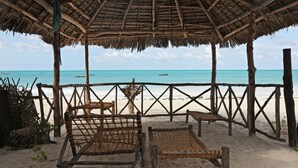 Un abri de plage avec un toit de chaume, des bancs en bois et une vue sur l’océan.