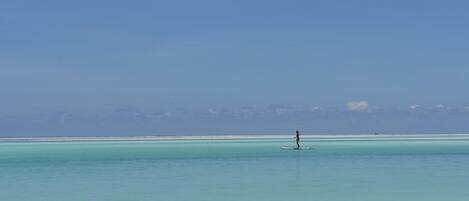 A person paddleboarding on clear turquoise waters with a distant shoreline.