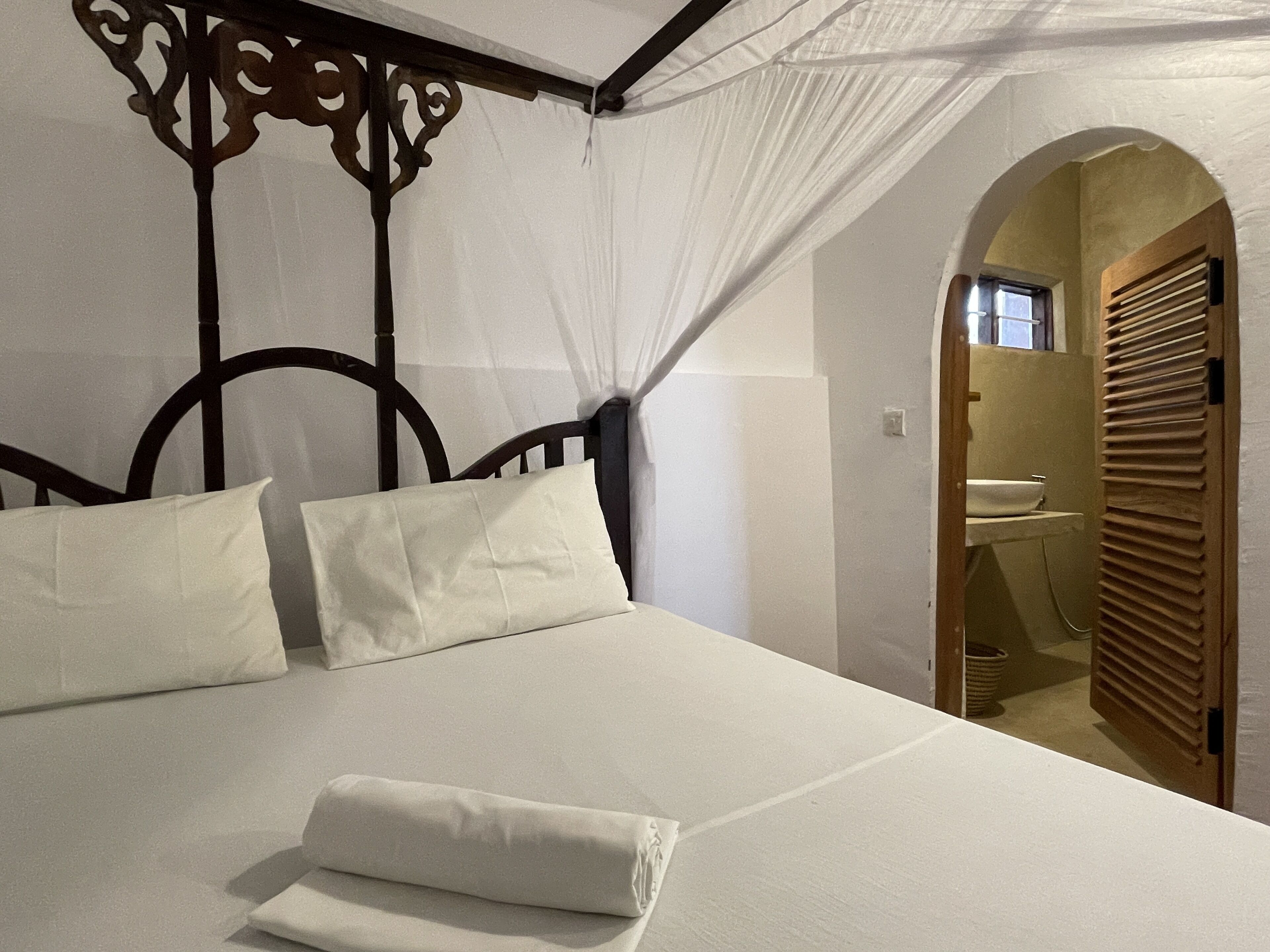 A neatly made bed with white linens, a wooden headboard, and a canopy.