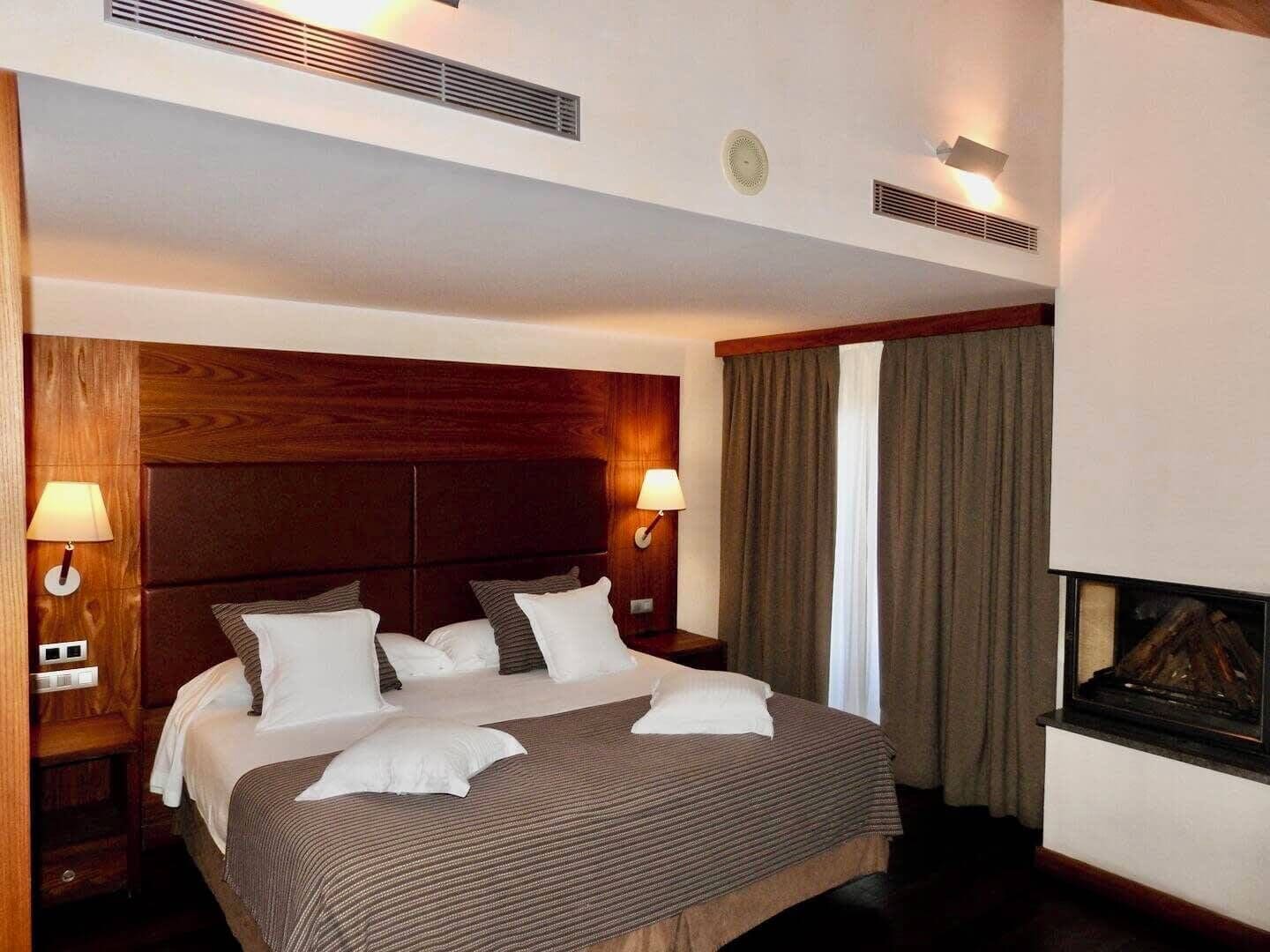 Una habitación de hotel con una cama grande, dos lámparas de noche, una chimenea y un cabecero de madera.