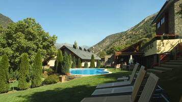 A pool area with lounge chairs, a stone building, and a mountainous backdrop.