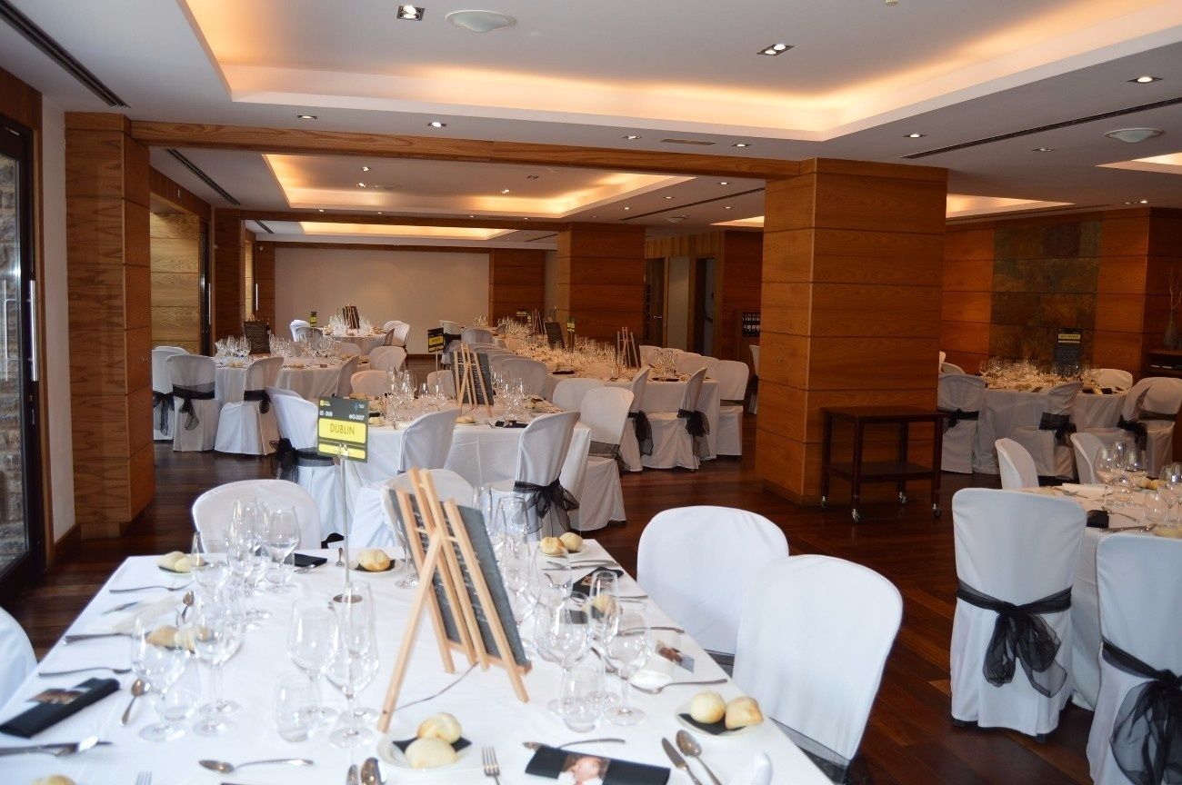 Una sala da banchetto con tavoli rotondi apparecchiati per un evento formale, con tovaglie bianche, bicchieri e posateria.