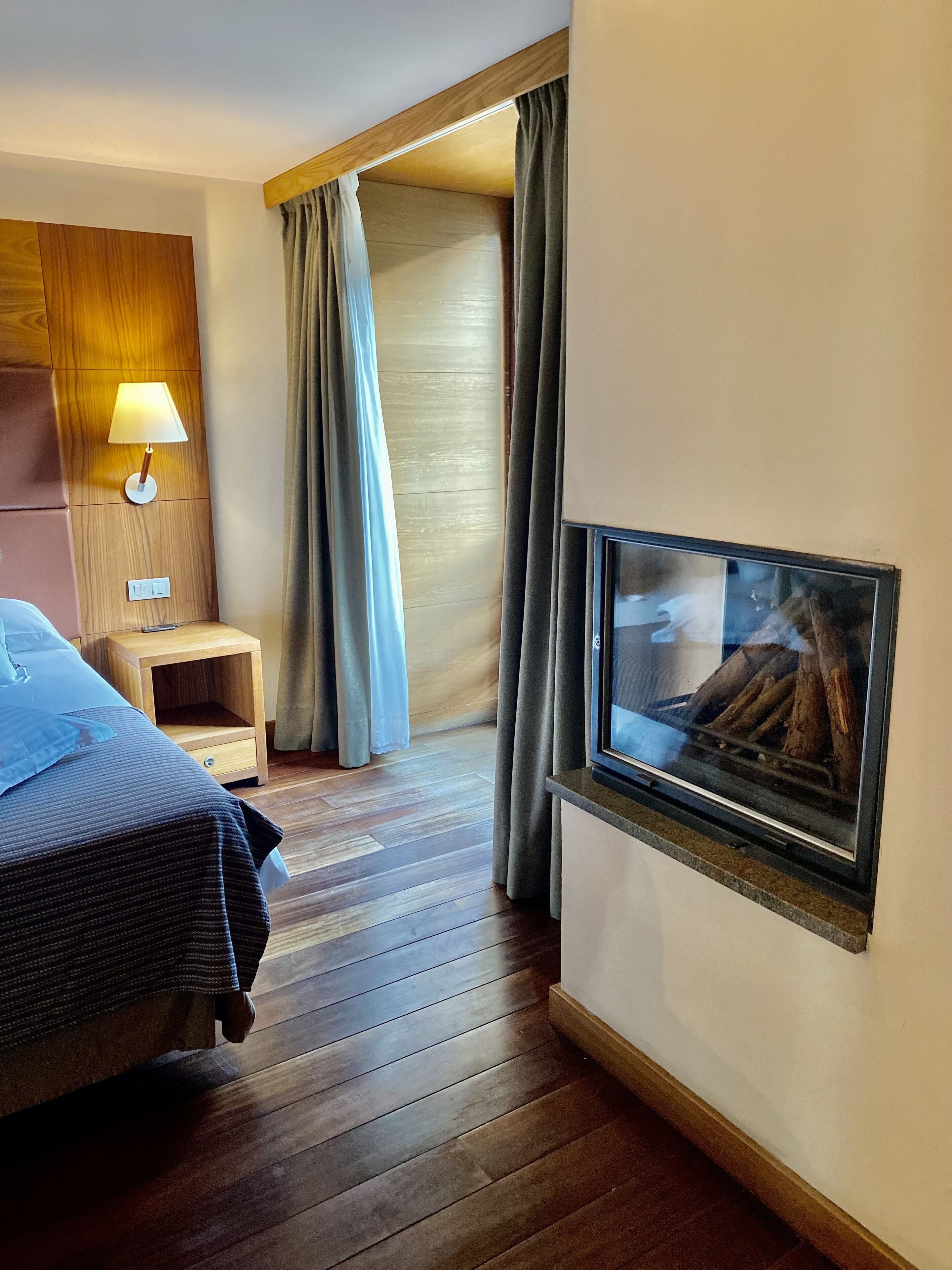 A hotel room with a bed, a nightstand, a lamp, a TV, and a window with curtains.