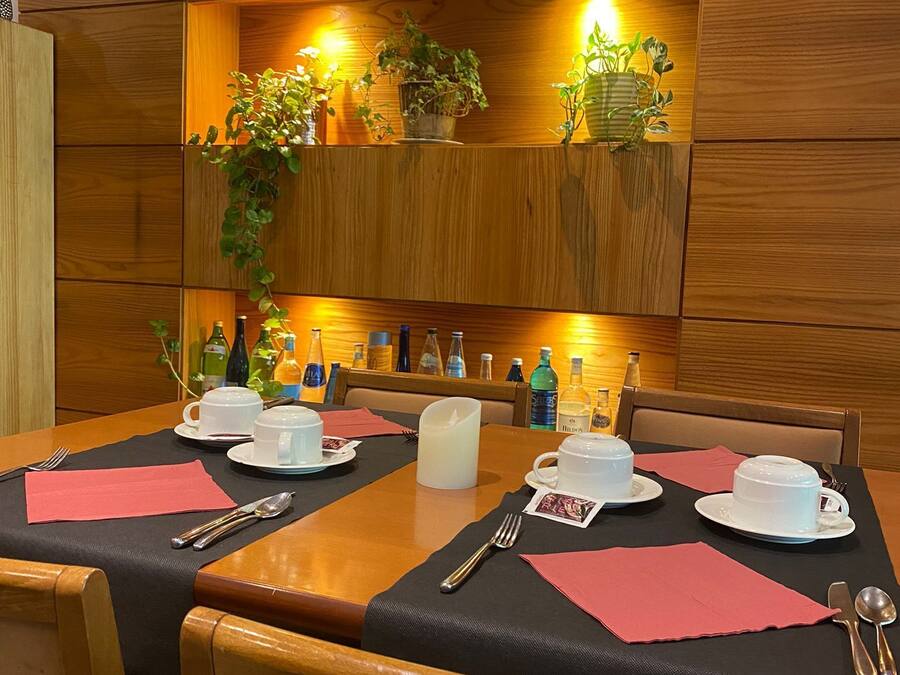 Una mesa de comedor dispuesta con tazas, platillos y una vela, rodeada de sillas de madera.