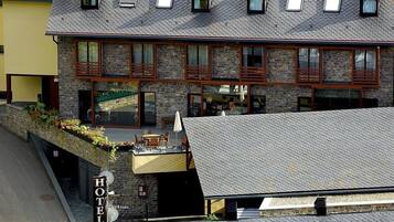 Un hotel con fachada de piedra, varias ventanas y una zona de estar al aire libre techada.