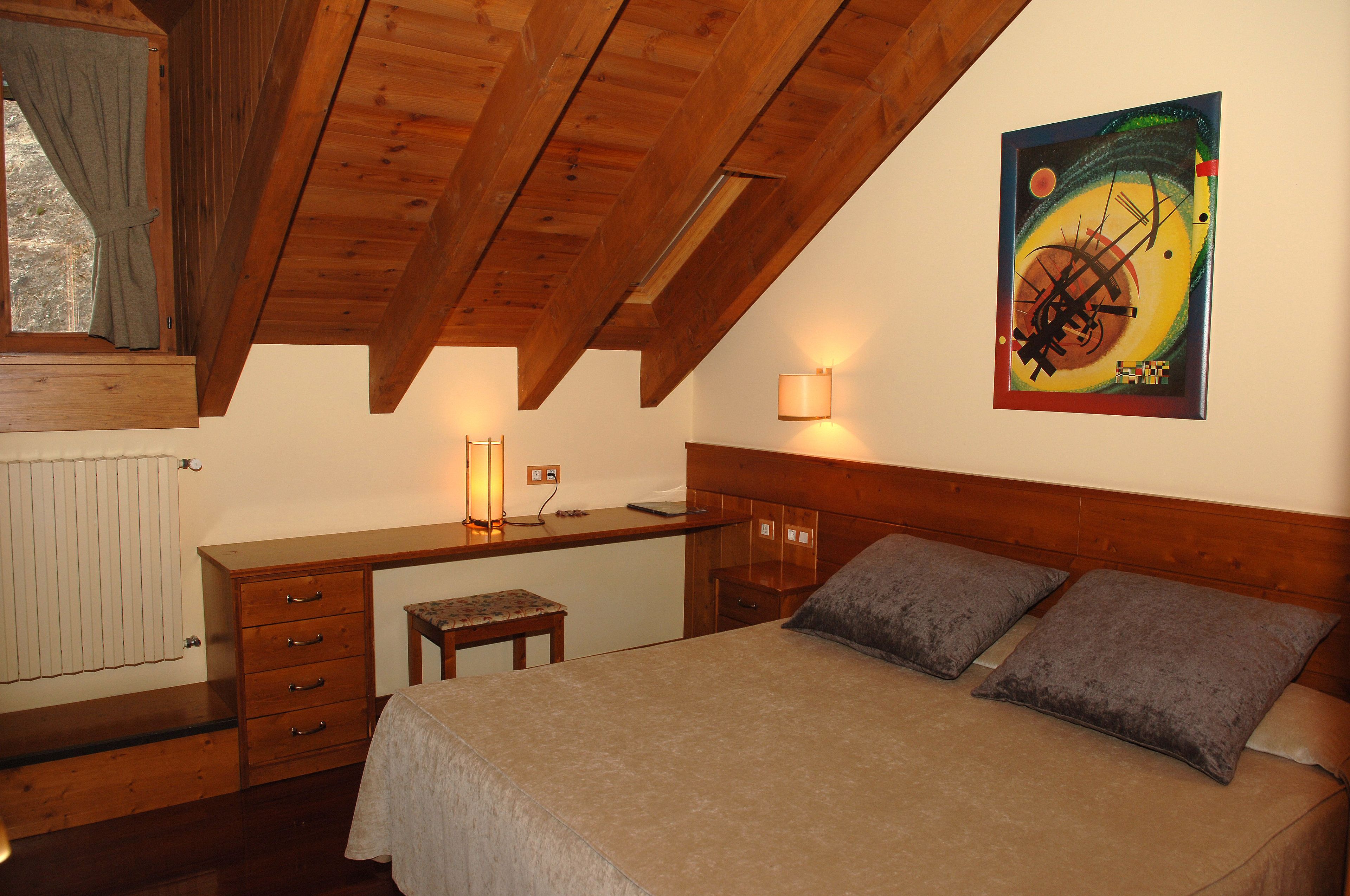 Une chambre avec un plafond en bois, un lit avec deux oreillers, un bureau avec une chaise et un tableau accroché au mur.