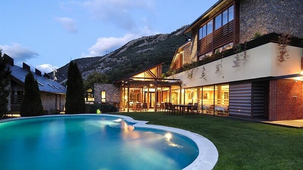 Ein modernes Haus mit Swimmingpool, Steinwänden und einem Berg im Hintergrund.
