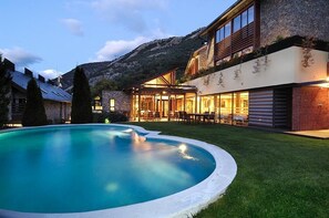 Una casa moderna con piscina, paredes de piedra y montañas al fondo.
