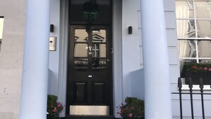 The entrance of The Beverley hotel with a black door, white columns, and a balcony with black railings. - The Beverley Hotel (London)