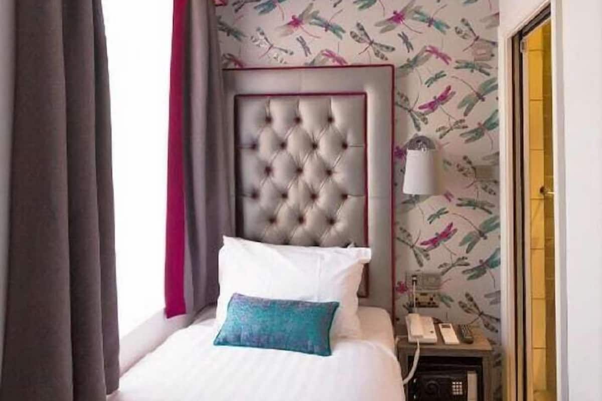 A hotel room with a bed, a nightstand, a telephone, and a window with curtains.