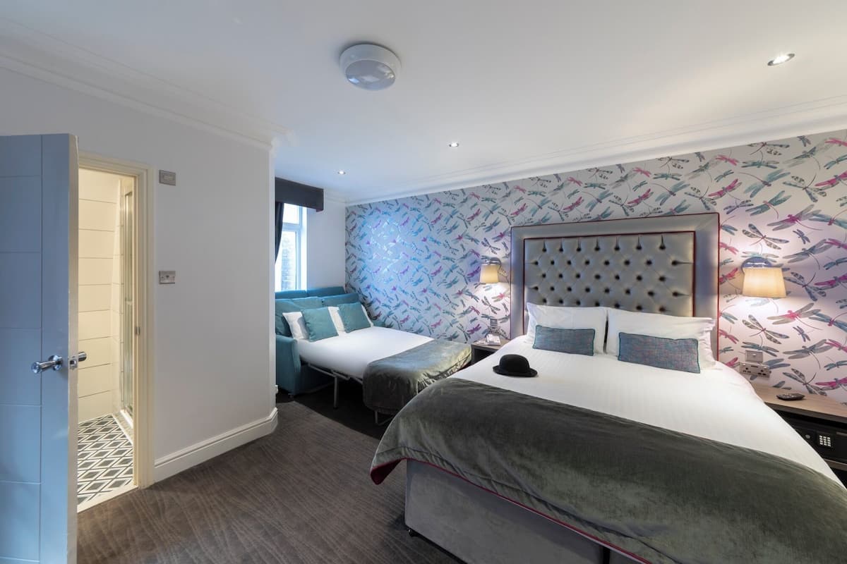 A hotel room with a large bed, a smaller sofa, and a window.