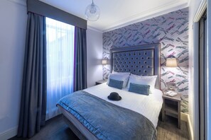 Une chambre d’hôtel avec un grand lit, une tête de lit capitonnée et un mur recouvert d’un papier peint à motifs de libellules.