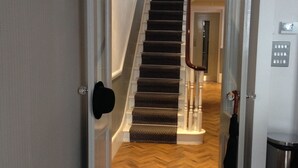 Un pasillo que conduce a una escalera, con alfombra estampada y suelo de madera.