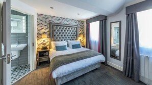 Una habitación de hotel moderna con una cama grande, una mesita de noche con lámpara, un espejo y vistas al exterior a través de una ventana.