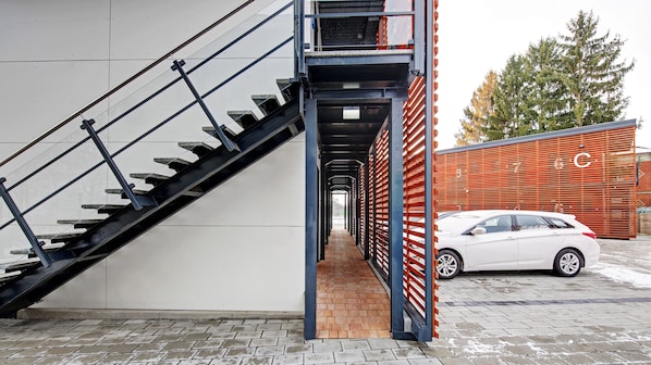 Un edificio moderno con una escalera que lleva a un segundo piso, un coche aparcado fuera y un camino de ladrillo.