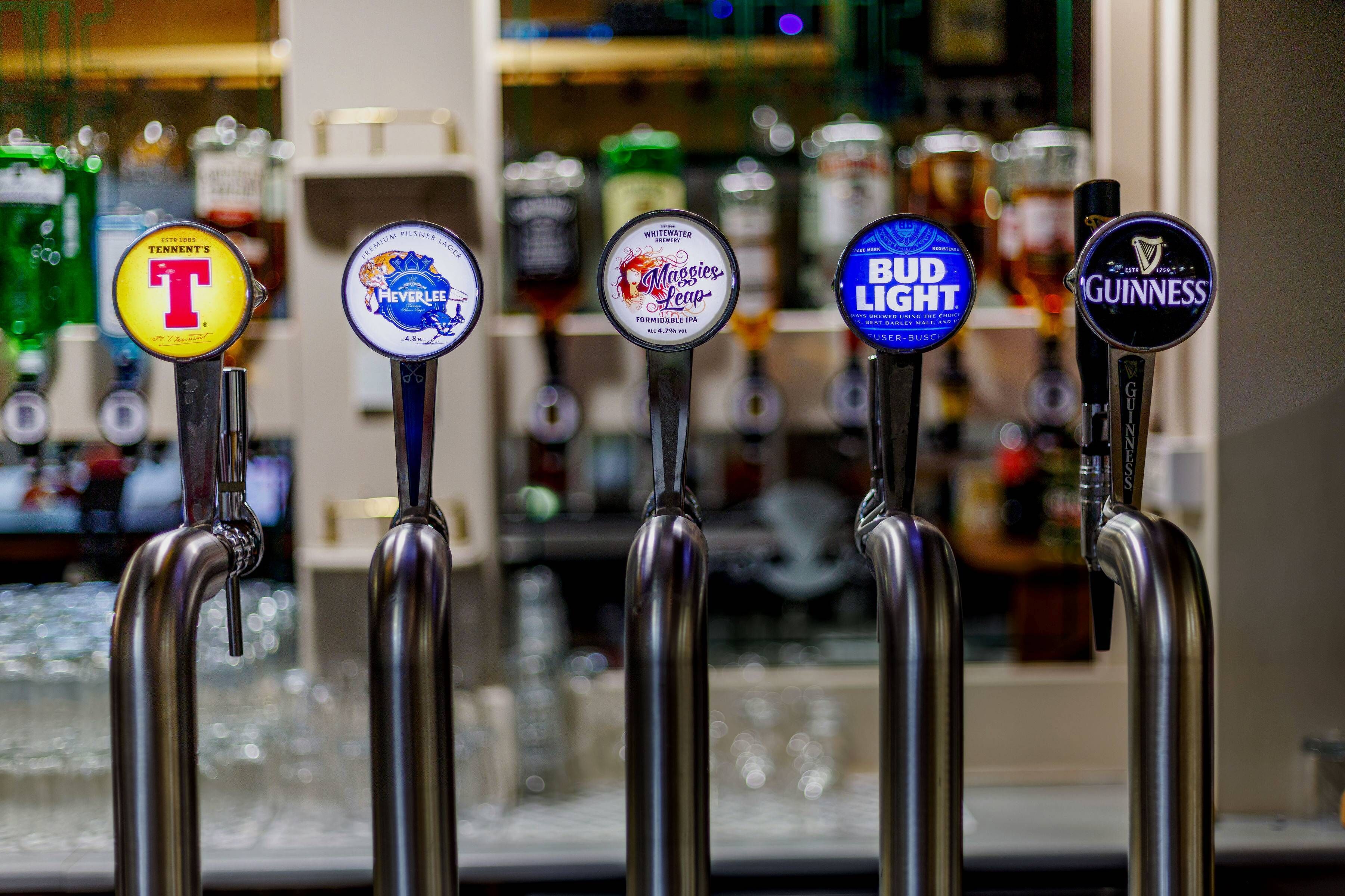 Una fila de grifos de cerveza con etiquetas que incluyen Tennent's, Heineken, Maggies Leap, Bud Light y Guinness.