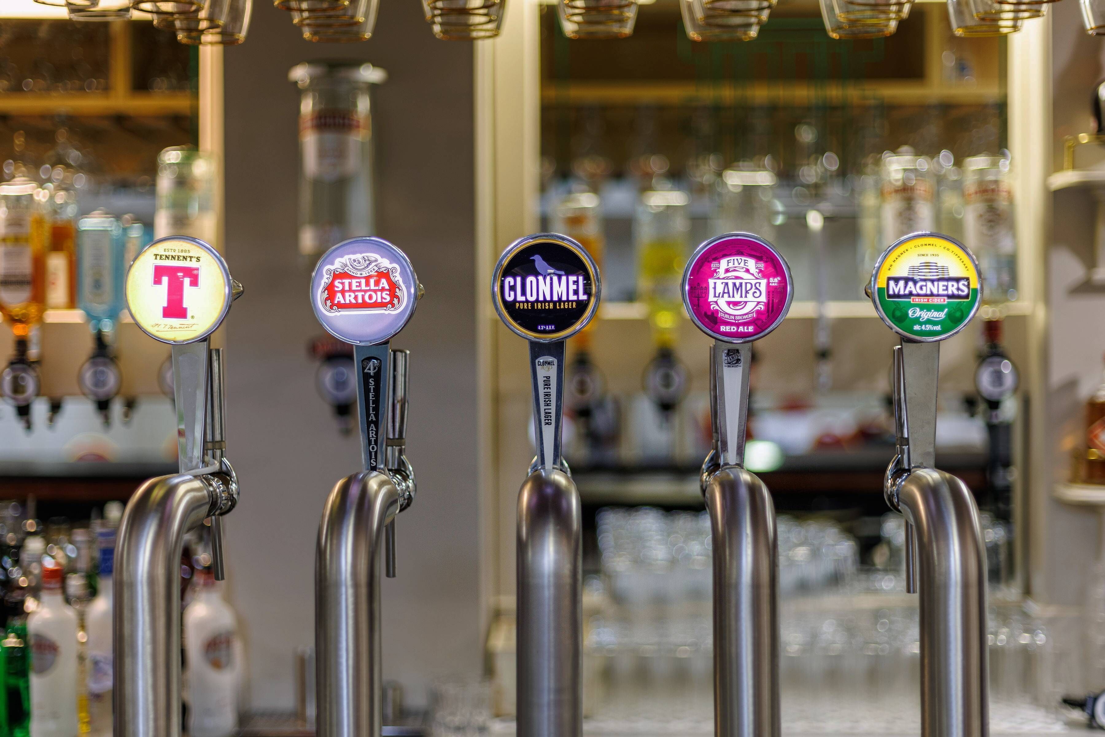 Una fila di rubinetti per la birra con etichette che includono Tennt's, Stella Artois, Clonmel, Lams e Magners.