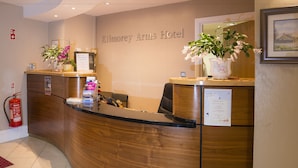 A reception desk at Kilmorey Arms Hotel with a wooden finish, a fire extinguisher, and two flower vases. - Kilmorey Arms Hotel (Newry)