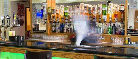 A bar area with multiple liquor dispensers, a digital screen, and bar stools.