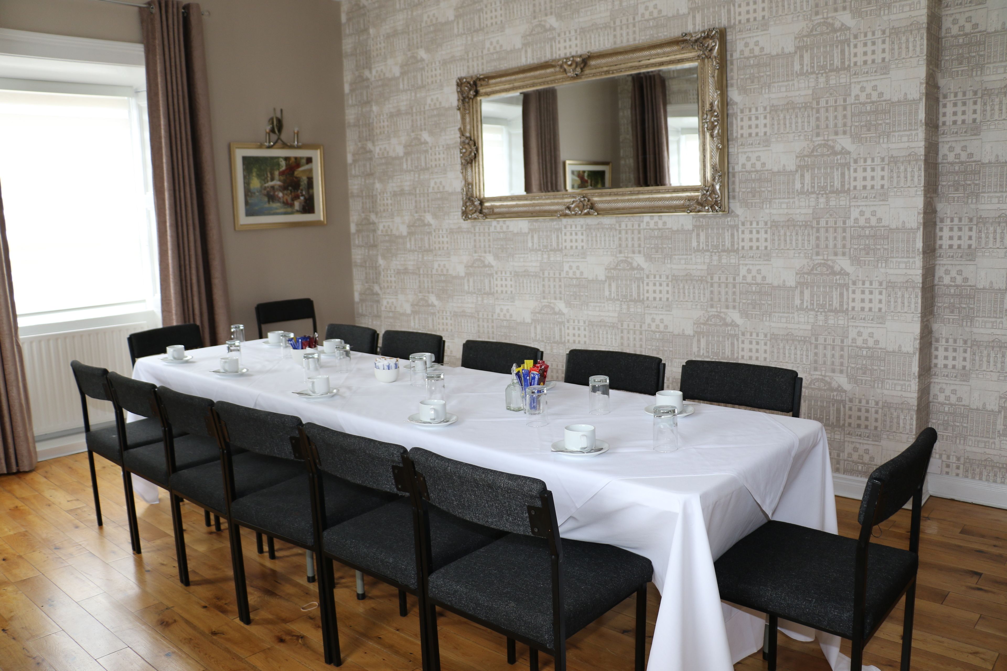 A conference room with a long table set for a meeting, surrounded by chairs, with a large mirror on the wall and a patterned wallpaper.