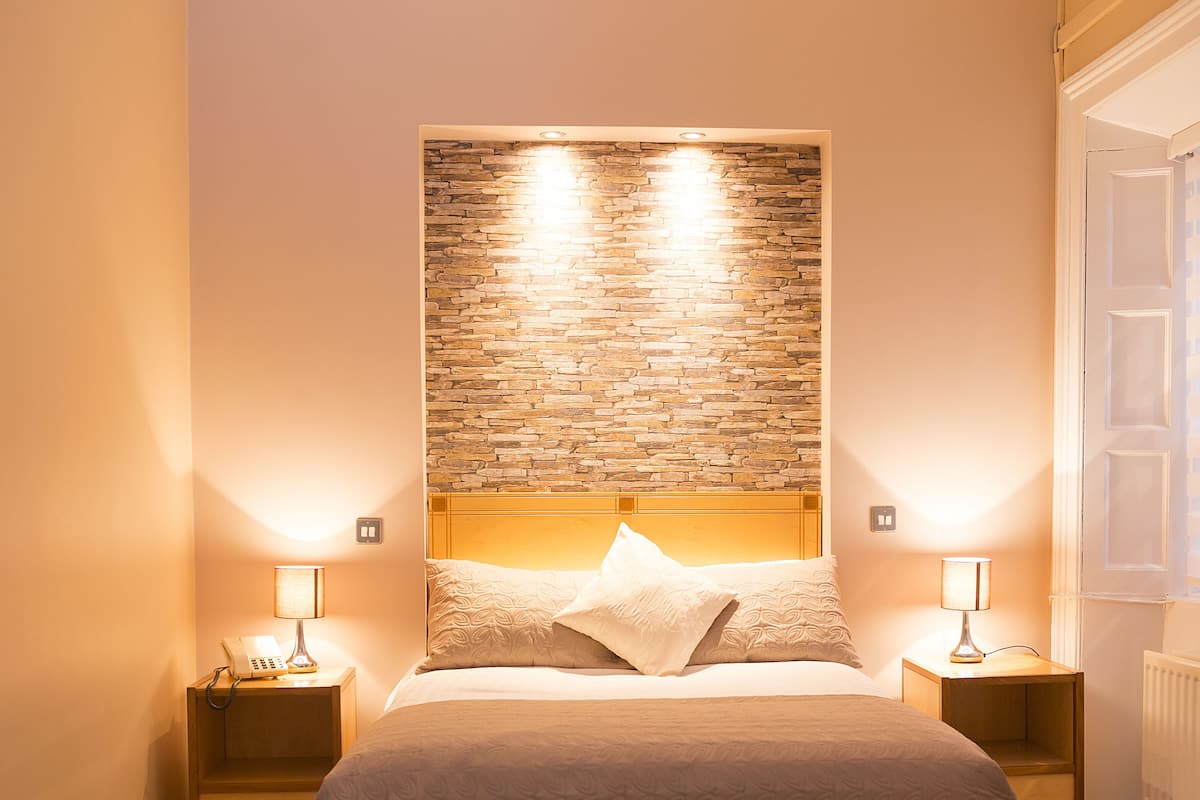 A bedroom with a large bed, two bedside tables with lamps, a stone-patterned headboard, and a radiator.