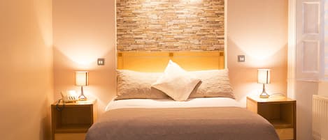Un dormitorio con una cama grande, dos mesitas de noche con lámparas, un cabecero con diseño de piedra y un radiador.