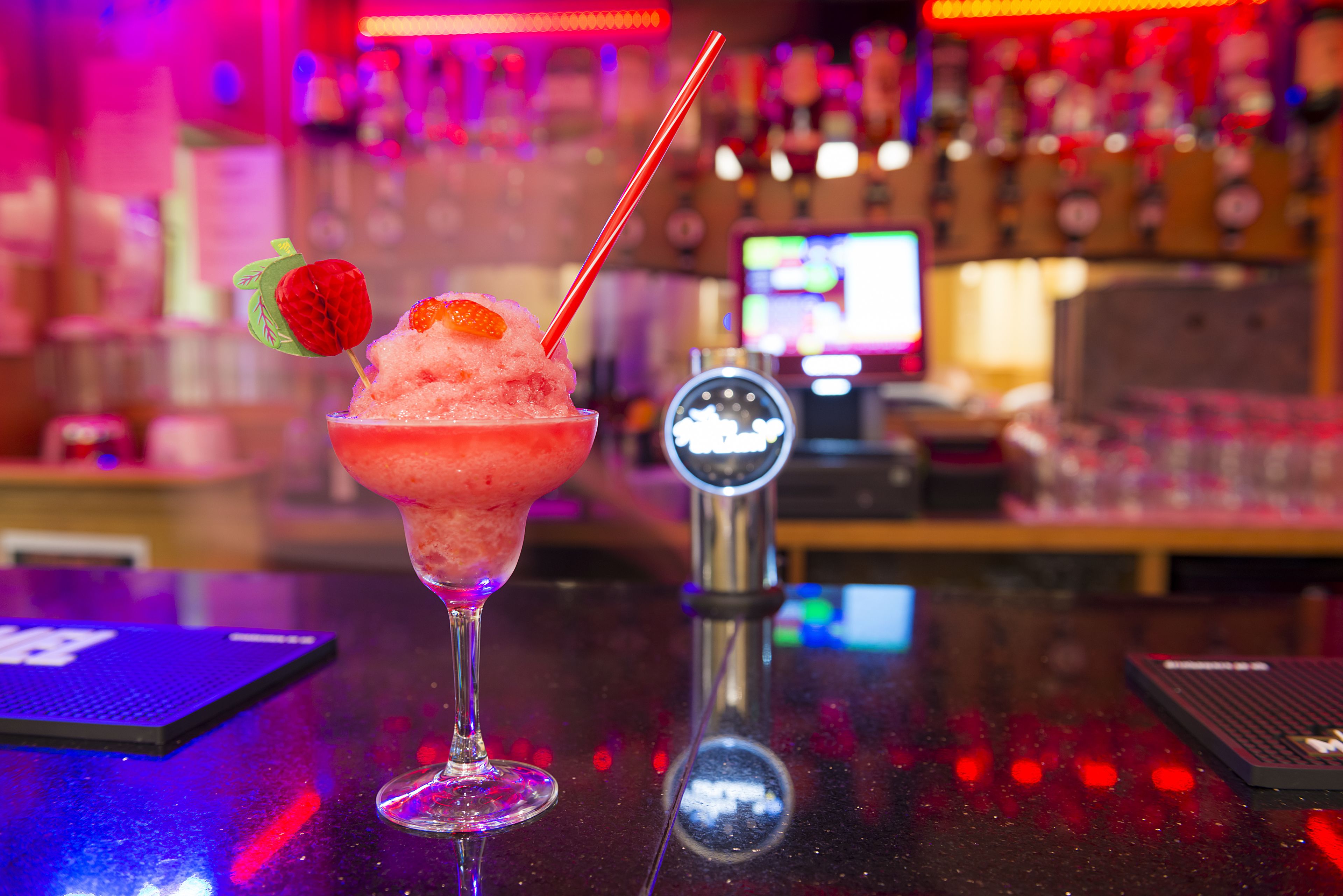 Un bar con un cóctel en un vaso, una balanza digital y un monitor de computadora al fondo.