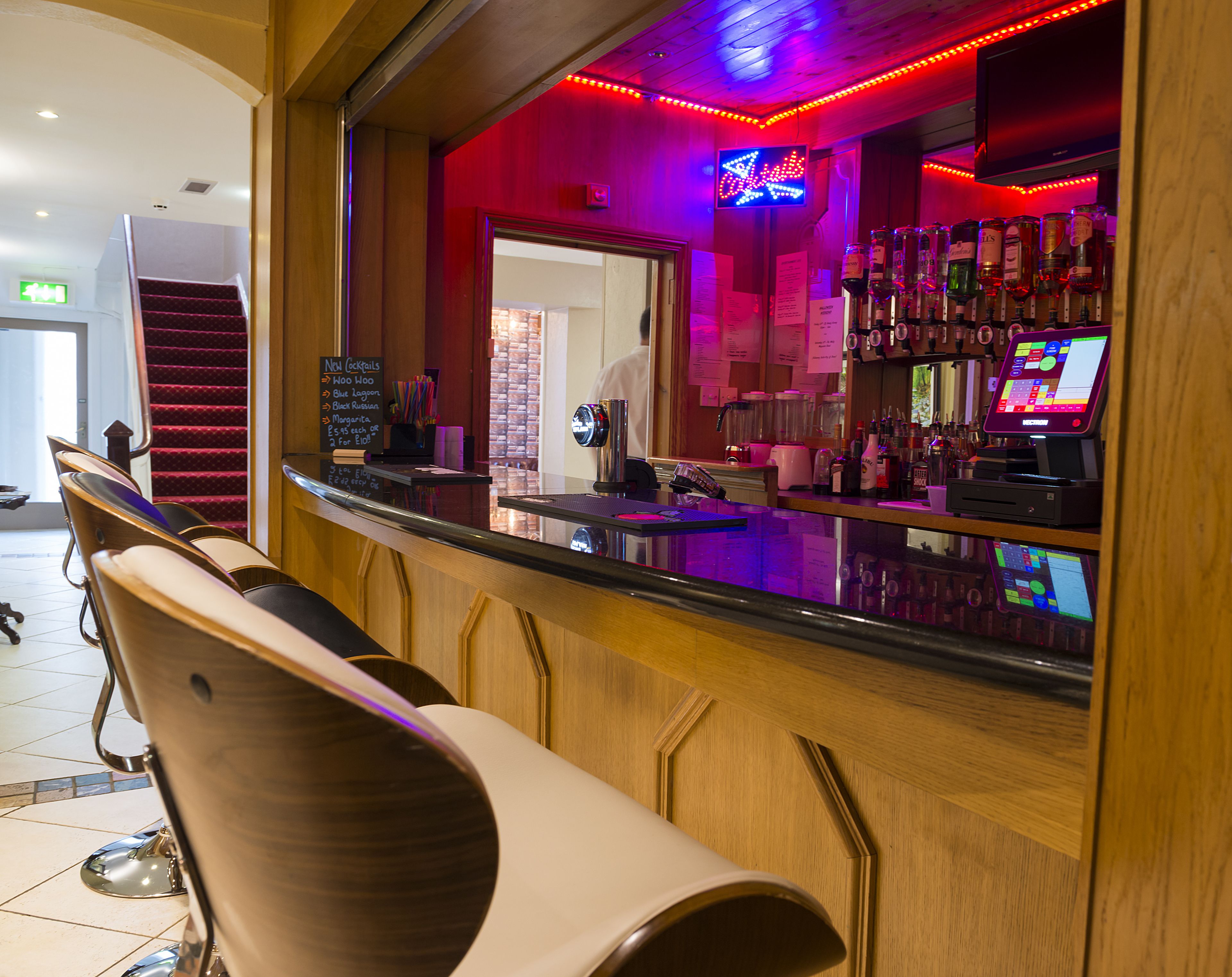 Eine Bar mit einer Theke, Barhocker und einem Neonzeichen.