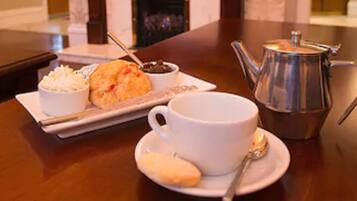 A table with a white cup, a teapot, a plate with a biscuit, and a small bowl of cream.